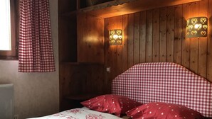 Un dormitorio con colcha a cuadros, almohadas rojas y cabecera de madera. Hay dos lámparas de pared con diseños de corazón.
