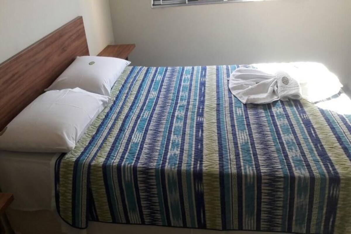 Una cama con colcha a rayas, dos almohadas y un cabecero de madera.