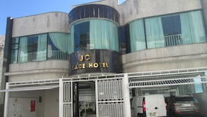Ein Hotel mit einer gewölbten Fassade, großen Fenstern mit Vorhängen und einem Schild mit der Aufschrift "JC Palace Hotel".