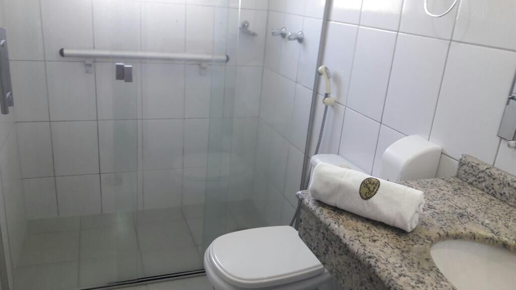 A bathroom with a glass-enclosed shower, a white toilet, and a granite countertop with a towel.