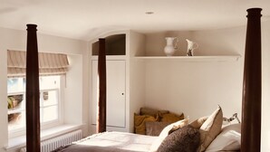 A bedroom with a four-poster bed, a window with a view, a radiator, and a shelf with decorative items. - 30% Discount Beautiful converted studio apartment in idyllic Cotswold village! (Cirencester)