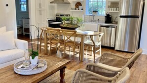 A modern kitchen with white cabinets, stainless steel appliances, and a dining area with wicker chairs and a wooden table.