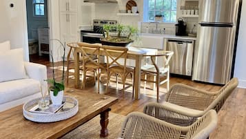 A modern kitchen with white cabinets, stainless steel appliances, and a dining area with wicker chairs and a wooden table.