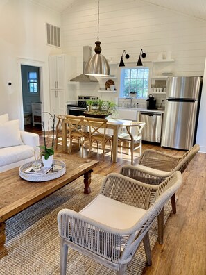 A modern kitchen with white cabinets, stainless steel appliances, and a dining area with wicker chairs and a wooden table.