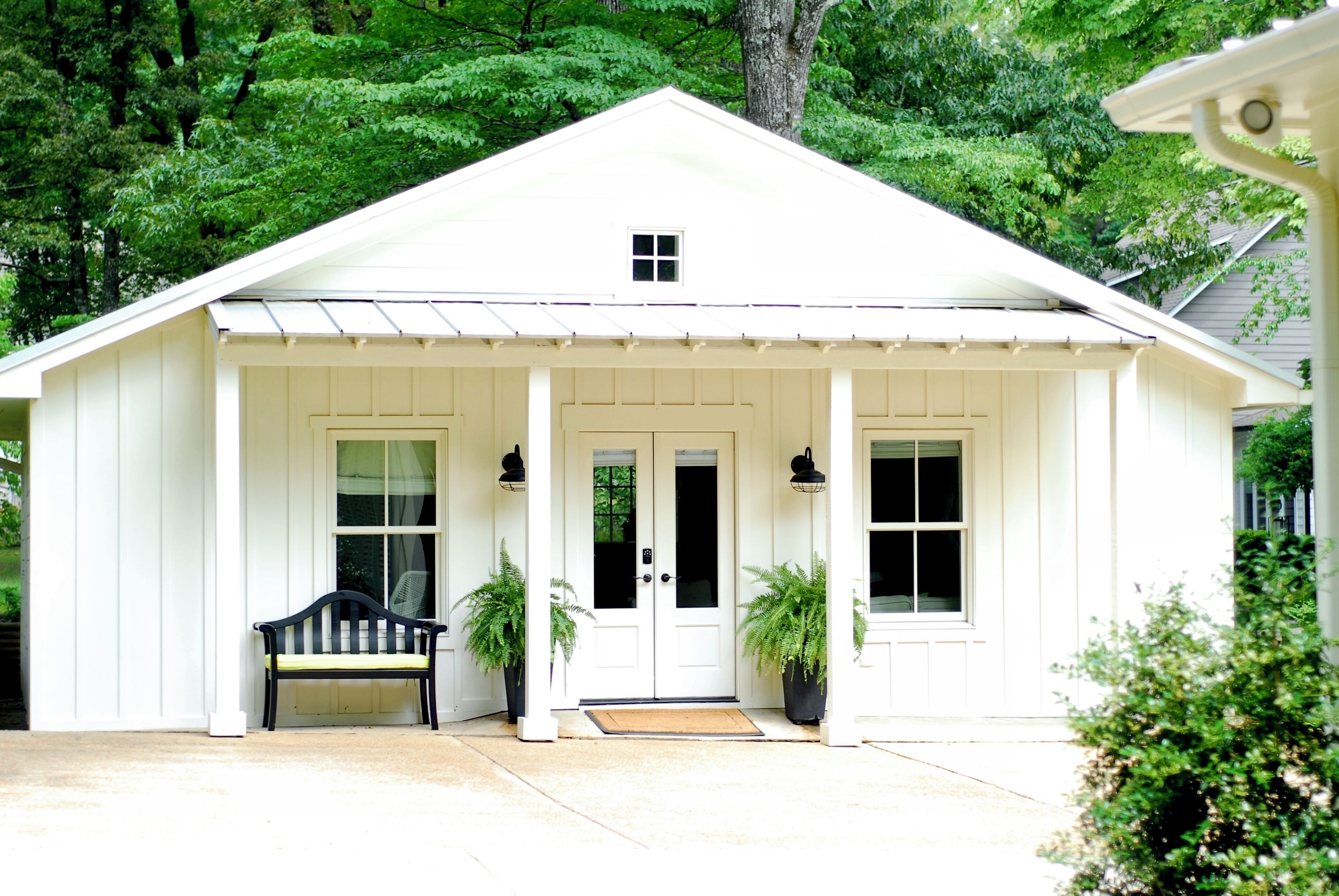 A white single-story house with a porch, a bench, and two potted plants.