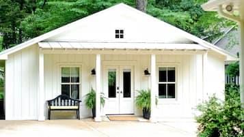 A white single-story house with a porch, a bench, and two potted plants.