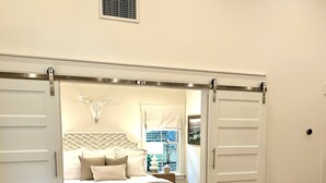A bedroom with a bed, a white couch, and a sliding door leading to another room.