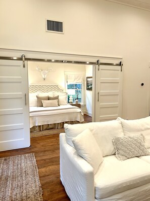 A bedroom with a bed, a white couch, and a sliding door leading to another room.