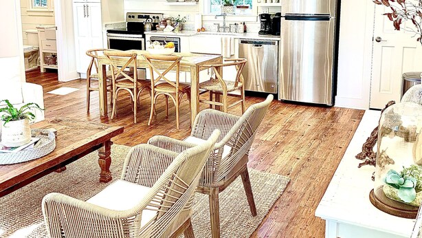 A spacious kitchen with white cabinetry, a stainless steel refrigerator, and a dining area with wicker chairs and a wooden table.