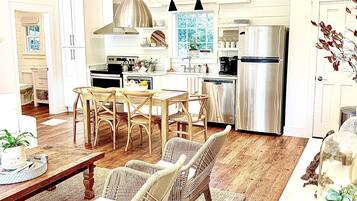 A spacious kitchen with white cabinetry, a stainless steel refrigerator, and a dining area with wicker chairs and a wooden table.