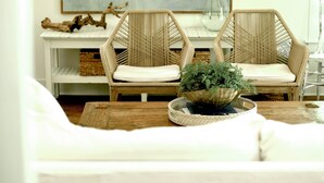 A living room with a white sofa, two wicker chairs, a coffee table with a plant, and a large abstract painting on the wall.