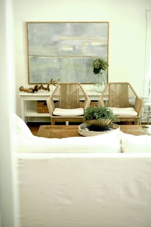 A living room with a white sofa, two wicker chairs, a coffee table with a plant, and a large abstract painting on the wall.