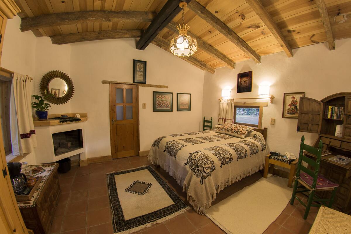Un dormitorio acogedor con techo de madera, una cama con ropa de cama estampada, una mesita con un teléfono y una silla.