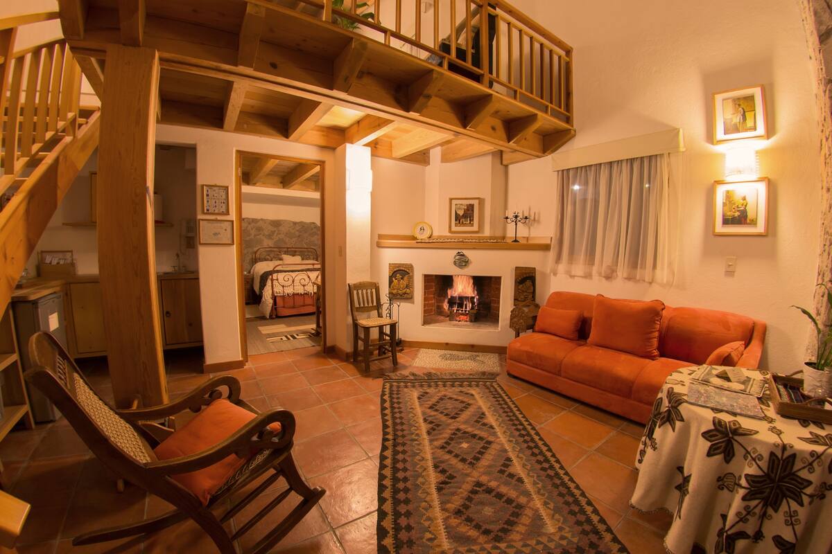 Una sala de estar acogedora con una escalera de madera, chimenea, sofá y una mesa de comedor.