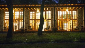Un bâtiment en pierre doté de grandes fenêtres et de poutres en bois, entouré d’arbres.