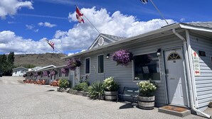 A row of single-story cabins with outdoor seating, a flagpole with flags, and a sign indicating the number of rooms. - The Orchard at Oliver (Oliver)