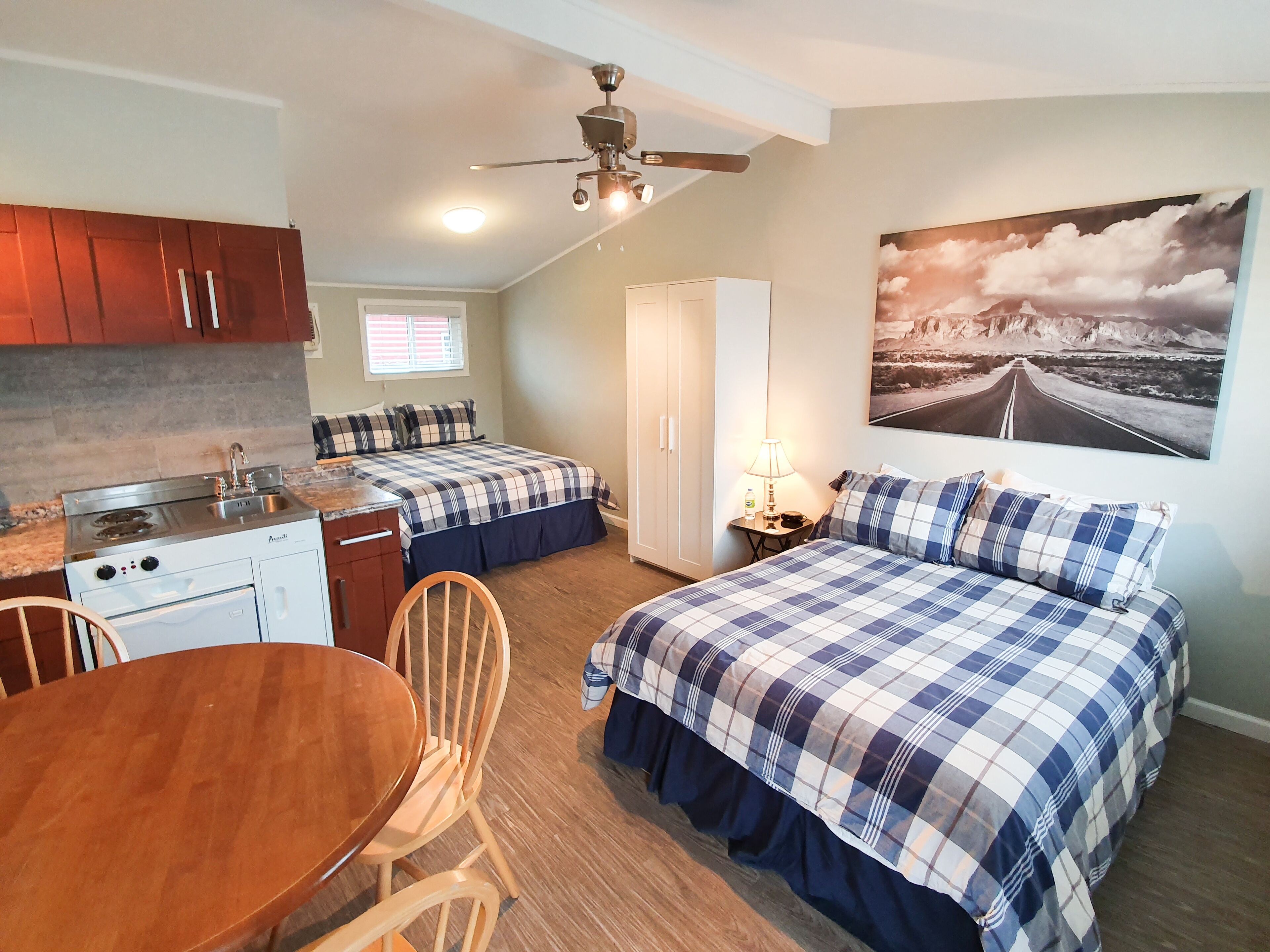 A compact room with a kitchenette, two beds with matching bedding, a dining table, and a ceiling fan.