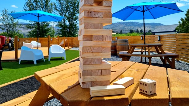 A wooden block game on a picnic table with a dice and two blue umbrellas in the background. - The Orchard at Oliver (Oliver)