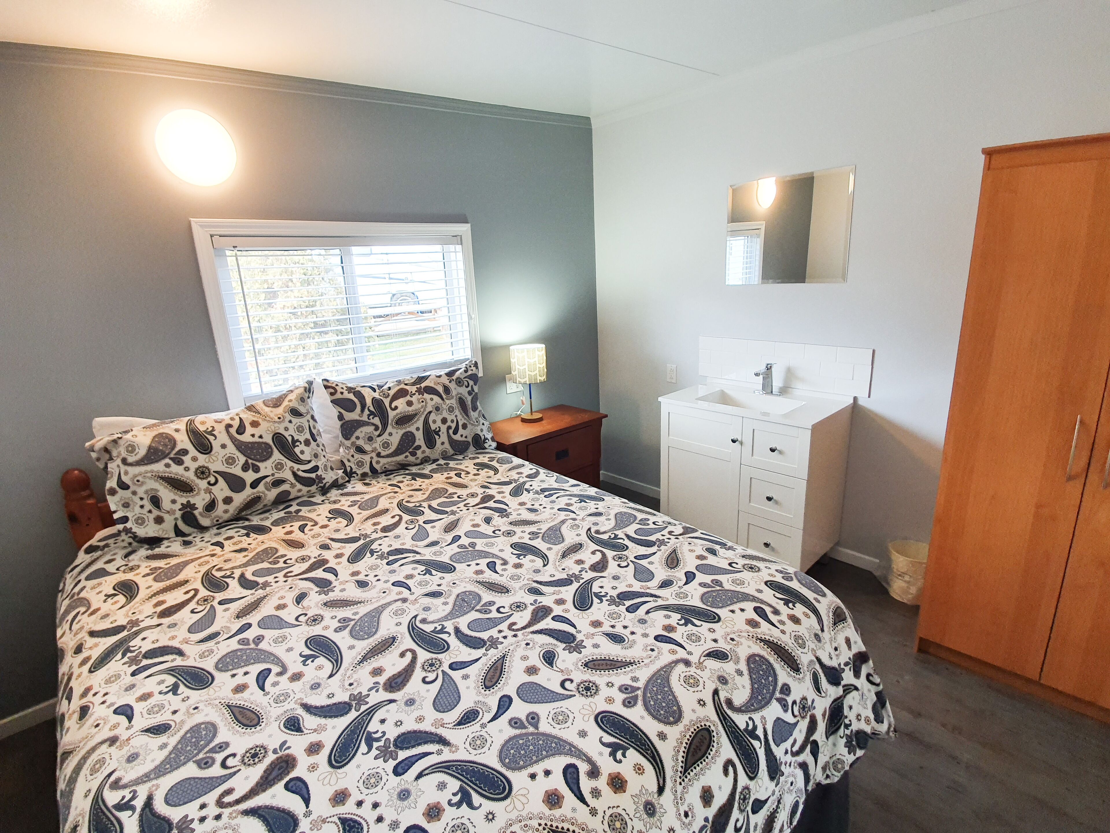 A bedroom with a bed, a nightstand, a dresser, a mirror, and a wardrobe.