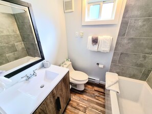 A bathroom with a wooden vanity, a large mirror, a toilet, and a bathtub. - The Orchard at Oliver (Oliver)