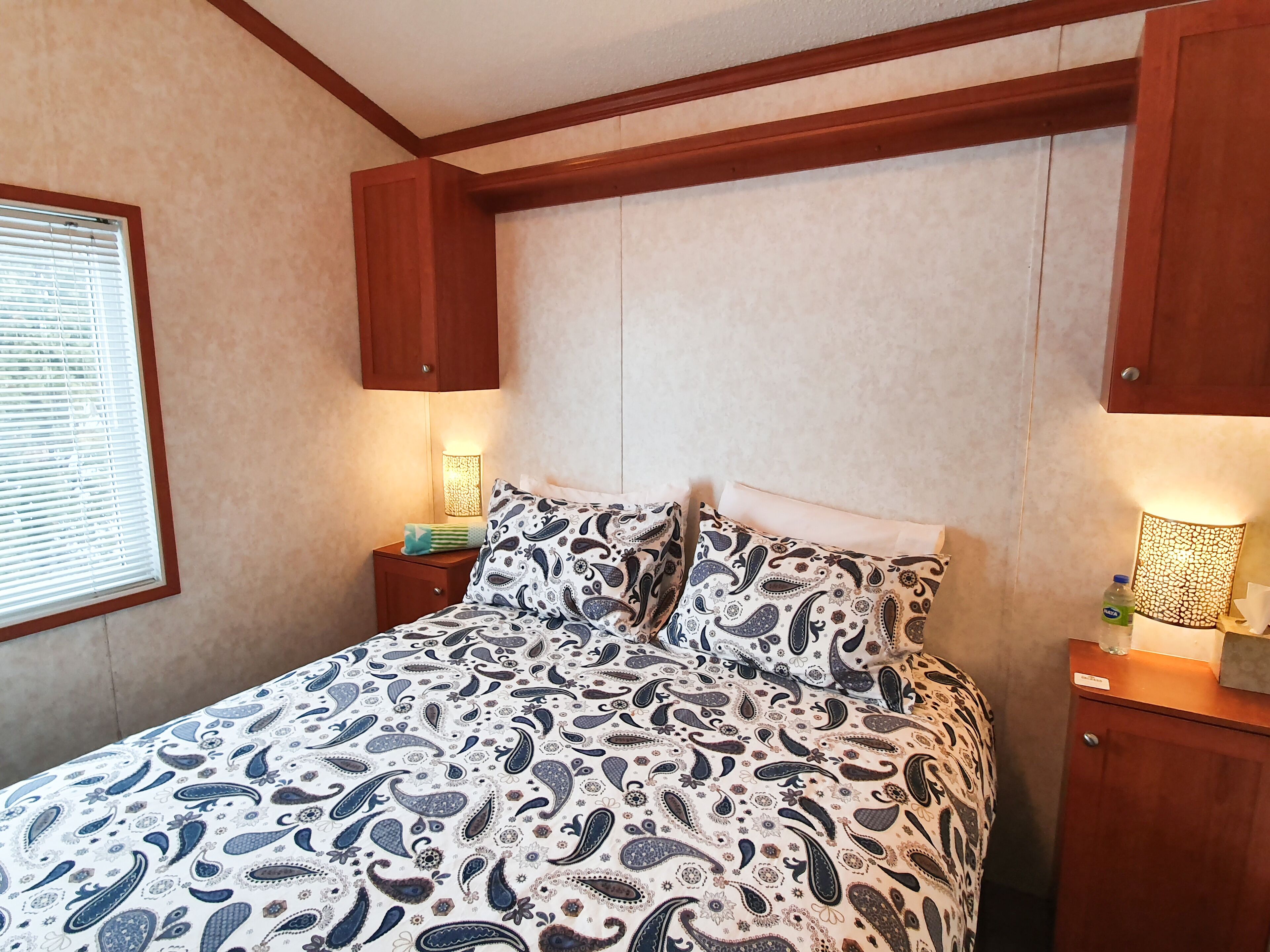 A bedroom with a bed, wooden headboard, bedside table with a lamp, and a nightstand.