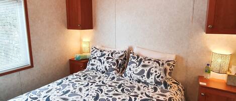 A bedroom with a bed, wooden headboard, bedside table with a lamp, and a nightstand.