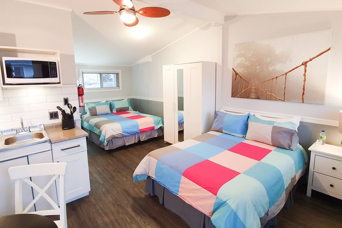 Habitación de hotel pequeña con kitchenette, dos camas, ventilador de techo y un gran ventanal.