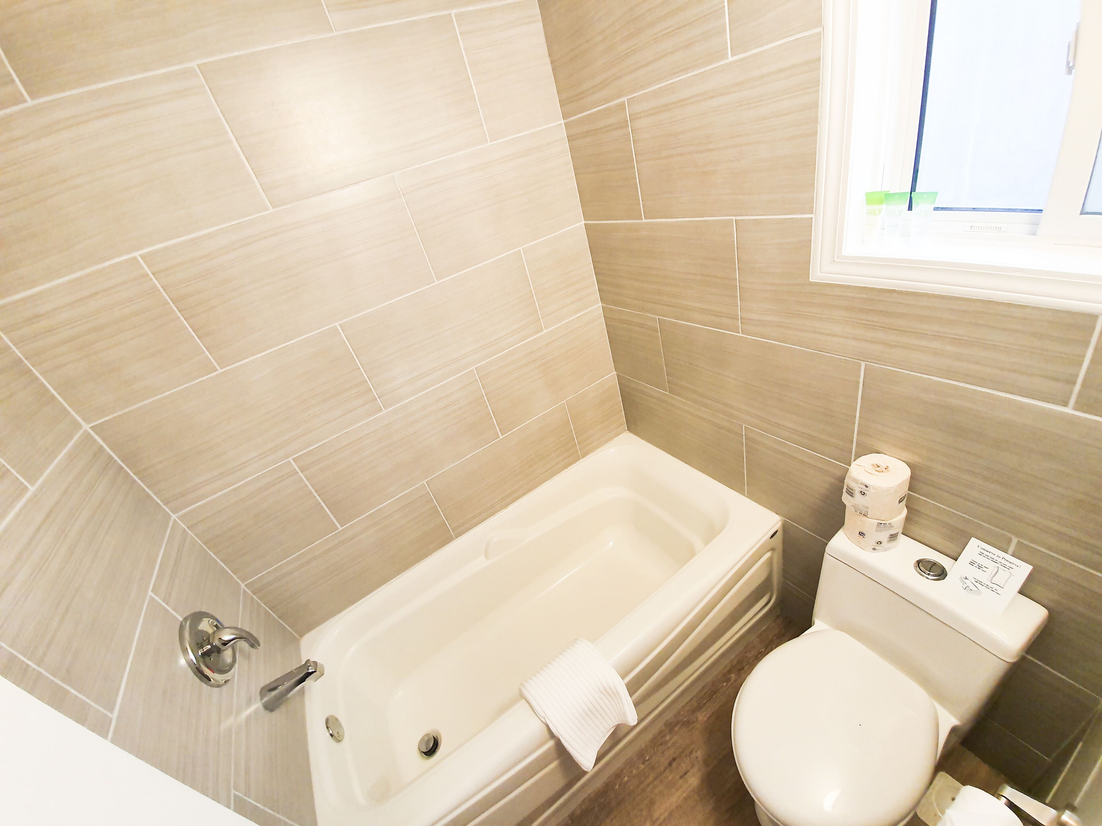 A bathroom with a bathtub, toilet, and a window.