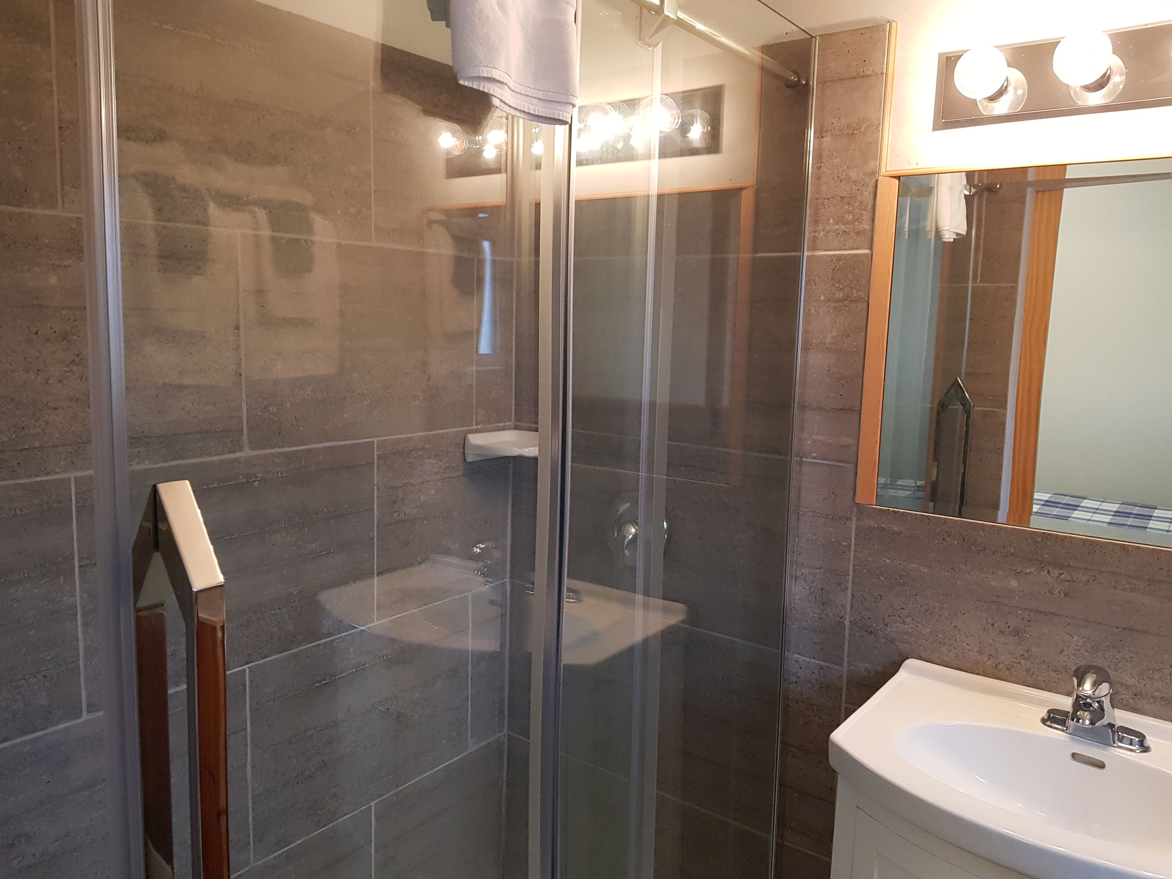 A modern bathroom with a glass-enclosed shower, a white sink, and a mirror with lights above it.