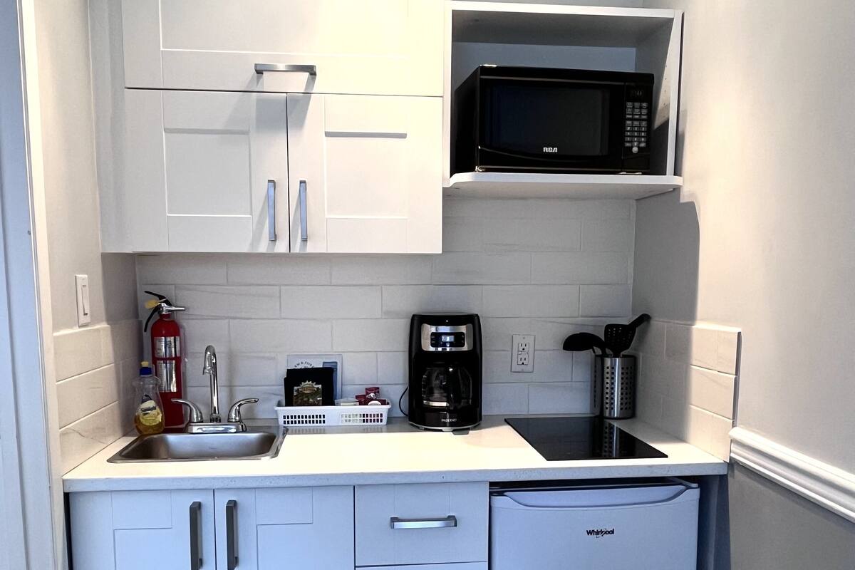 Una cocina compacta con armarios blancos, microondas, cafetera y lavavajillas.