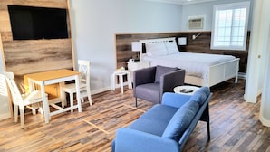 A bedroom with a bed, a desk, a chair, a sofa, and a TV mounted on the wall. - The Orchard at Oliver (Oliver)