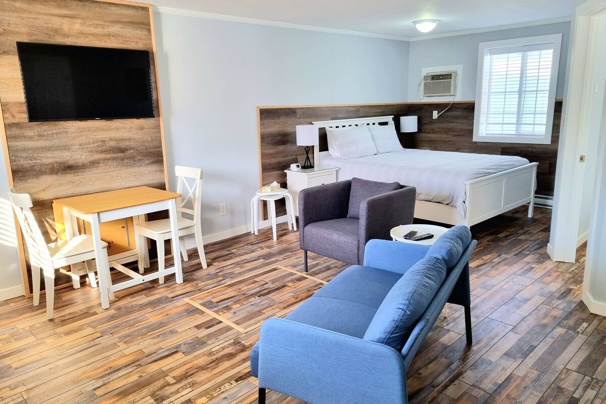 Un dormitorio con cama, escritorio, silla, sofá y televisor fijado a la pared.