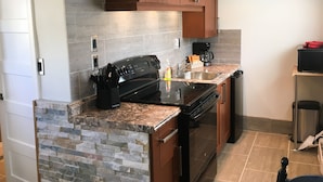 A kitchen with granite countertops, a stove, a coffee maker, and wooden cabinets. - The Orchard at Oliver (Oliver)