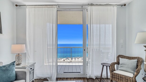 Habitación con balcón que da a una playa, una silla de mimbre, una mesita y un sofá.