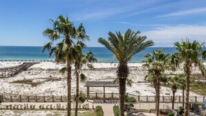 Vista a la playa con palmeras, una terraza de madera y un pabellón.
