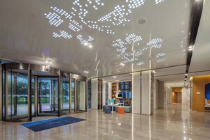 A modern lobby with a glass entrance, a reception desk, and a seating area with a blue carpet.