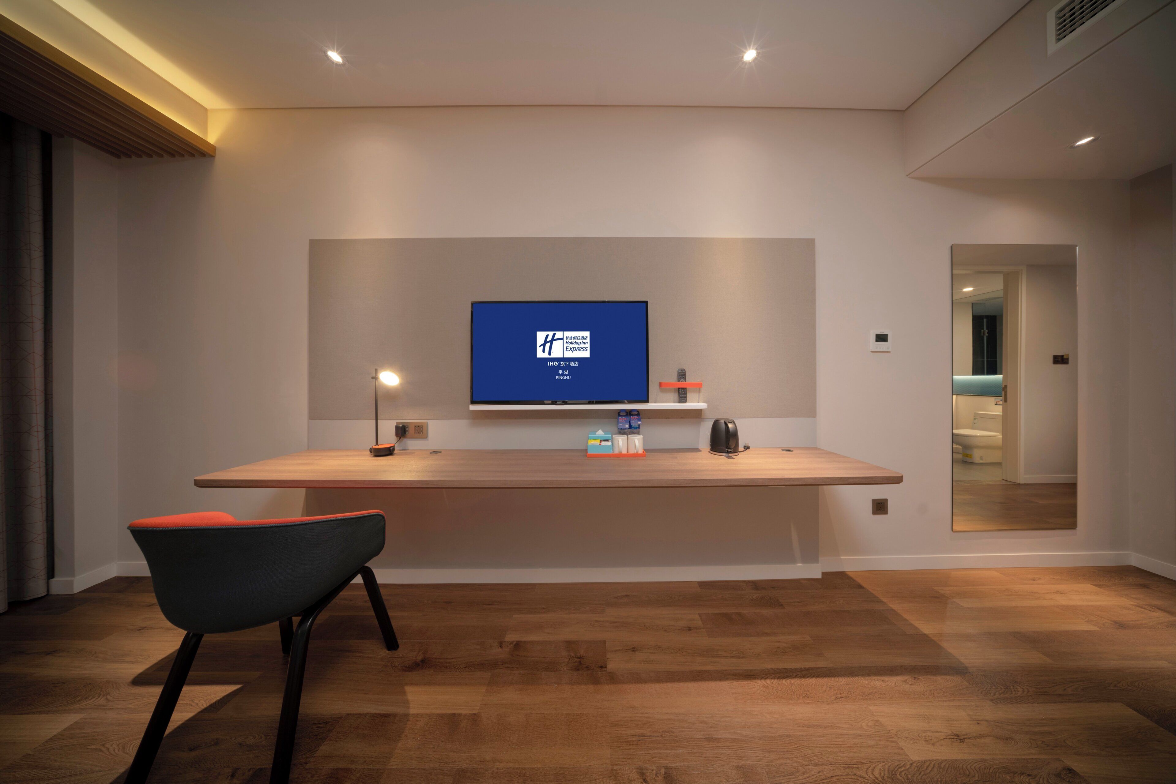 Una habitación de hotel moderna con un mostrador de recepción de madera, un televisor de pantalla plana montado en la pared, una cafetera y una silla.