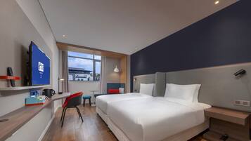 A modern hotel room with a large bed, a desk with a chair, a TV, and a window with a view of the outside.