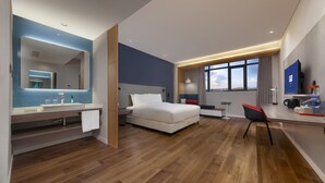 A modern hotel room with a wooden floor, a large bed, a desk with a chair, a TV, and a bathroom with a mirror and sink. - Holiday Inn Express Pinghu by IHG (Jiaxing)
