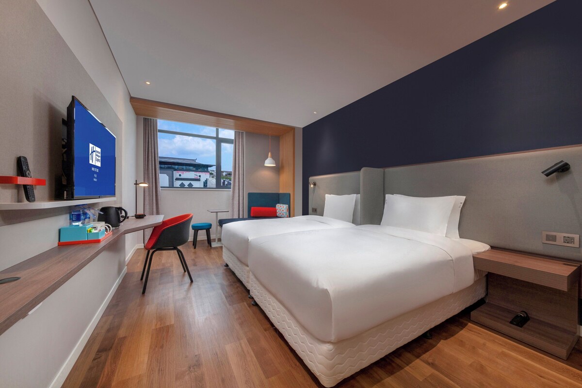 Ein Hotelzimmer mit Bett, Schreibtisch, Stuhl, Fernseher und Fenster.