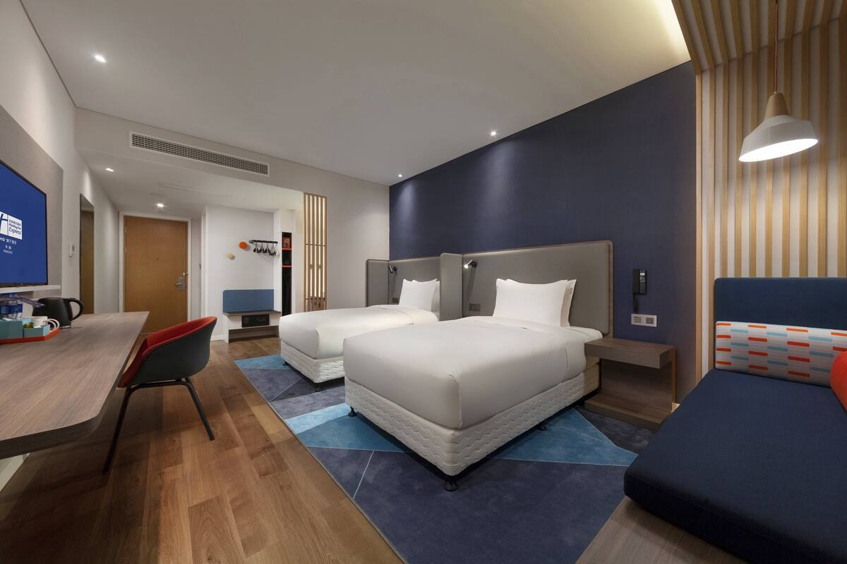 A hotel room with two beds, a desk, and a seating area.