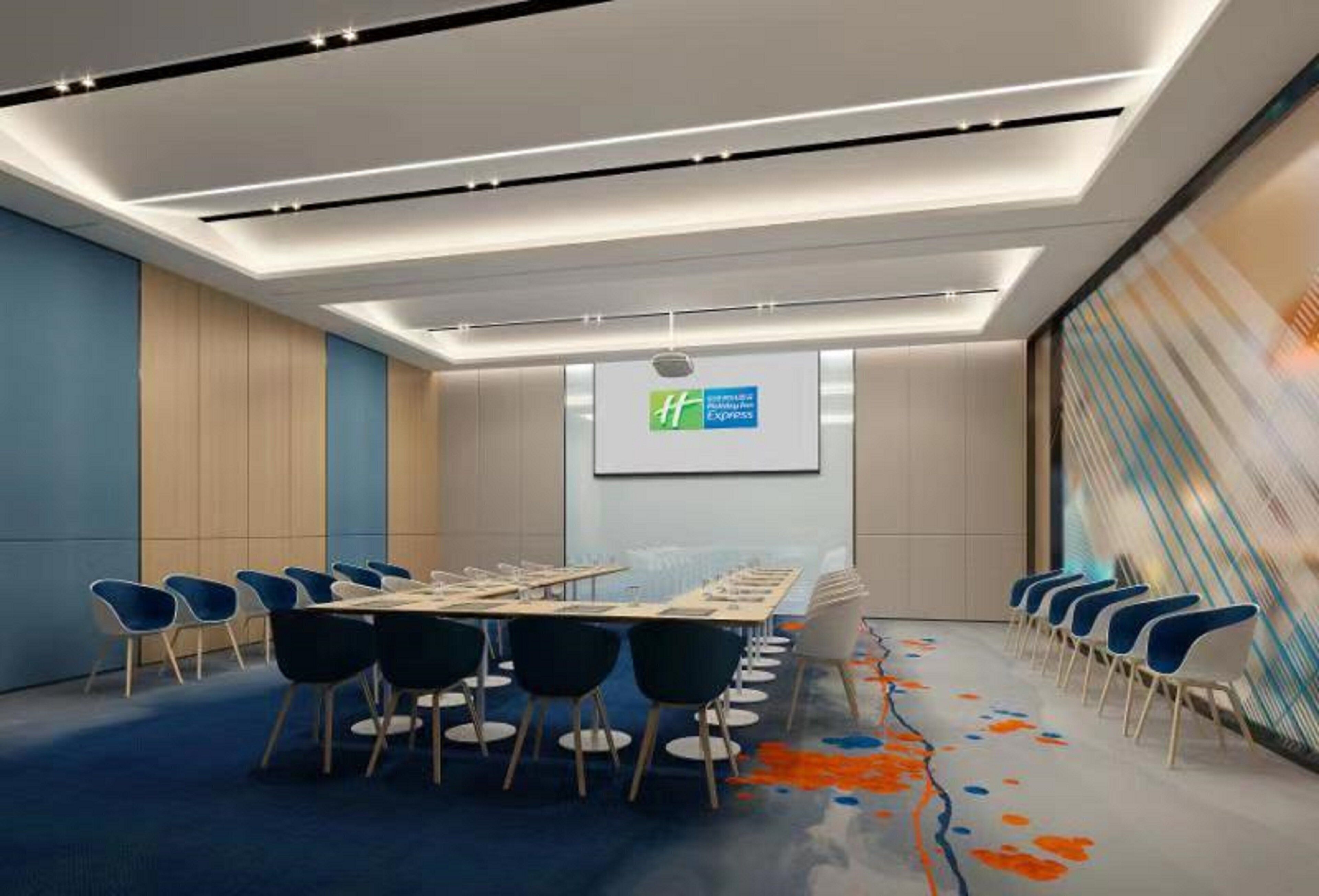 Una sala de conferencias moderna con una larga mesa, sillas azules y una pantalla grande que muestra un logotipo.