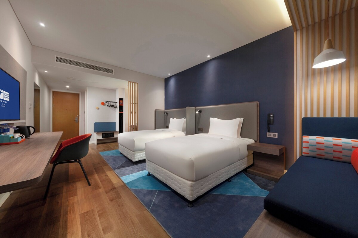 Ein Hotelzimmer mit zwei Betten, einem Schreibtisch, einem Stuhl, einem Fernseher und einem Badezimmer.