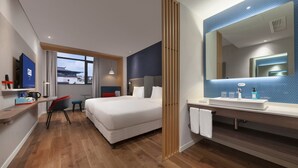 A hotel room with a bed, a desk, a chair, a large mirror, a bathroom with a sink and mirror, and a window with a view. - Holiday Inn Express Pinghu by IHG (Jiaxing)