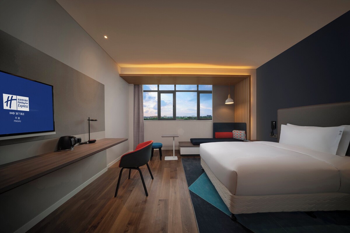 Ein Hotelzimmer mit Bett, Schreibtisch, Stuhl, Fernseher und Blick auf die Stadt.