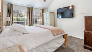 Un dormitorio con cama, ventilador de techo, televisor montado en la pared y ventana con cortinas.