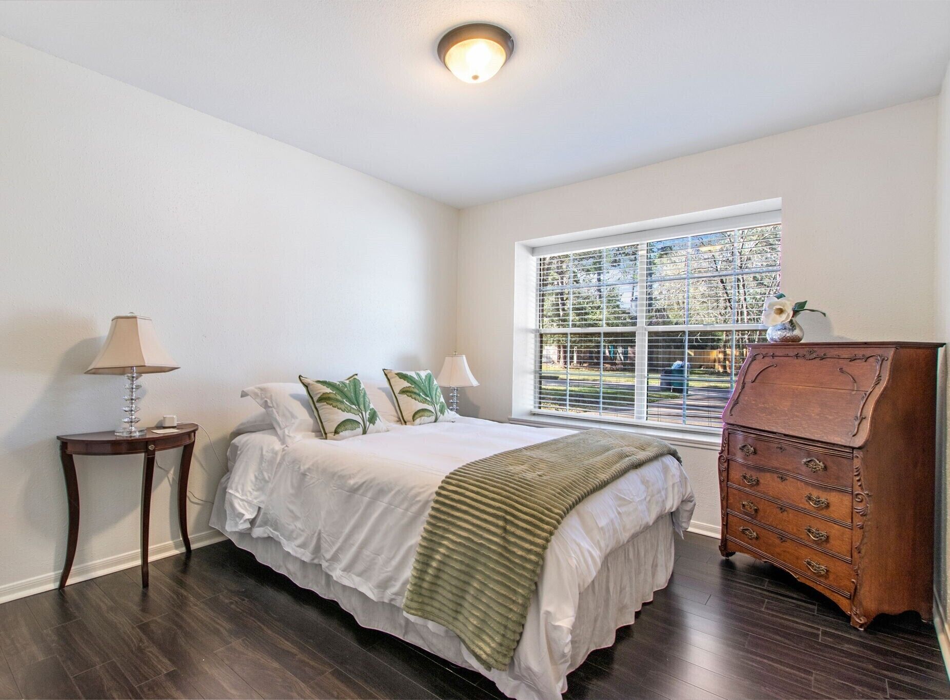 A bedroom with a bed, a nightstand, a dresser, and a window with blinds.