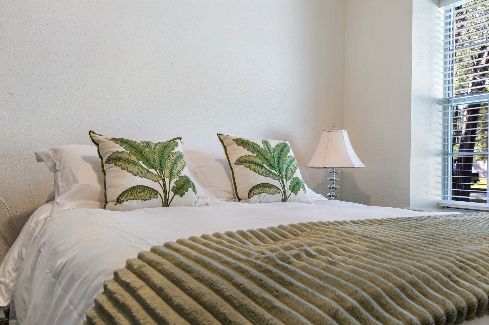 Un letto ben rifatto con lenzuola bianche e due cuscini decorativi a motivi floreali.