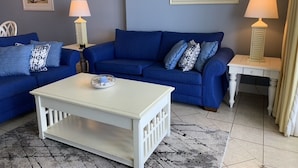 Een woonkamer met een blauwe zithoek, een witte salontafel en twee lampen.