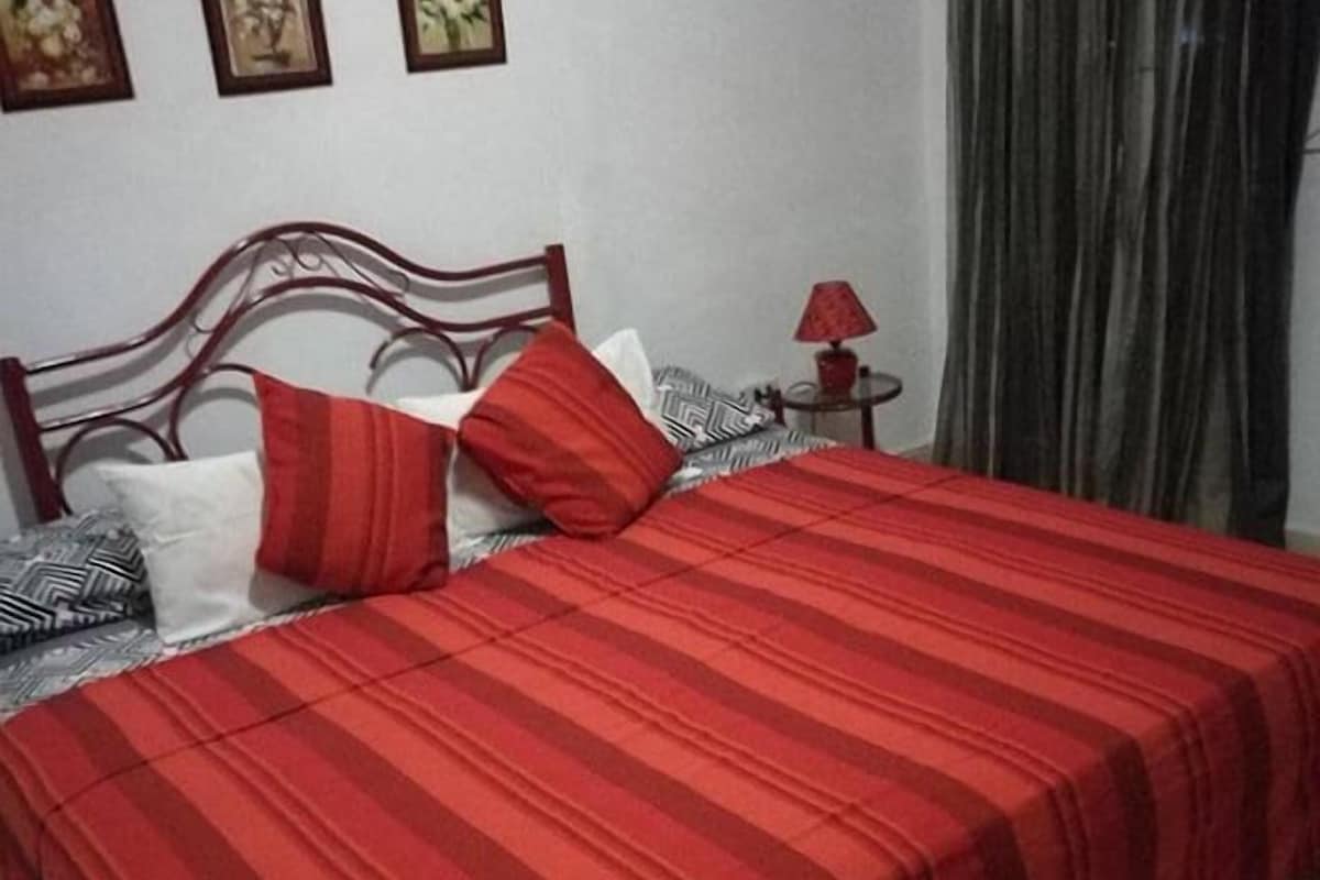 A neatly made bed with a red striped bedspread, a wooden headboard, and a small bedside table with a lamp.